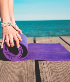 Young beautiful sporty woman preparing for yoga asana on sea beach near water. Girl covering purple